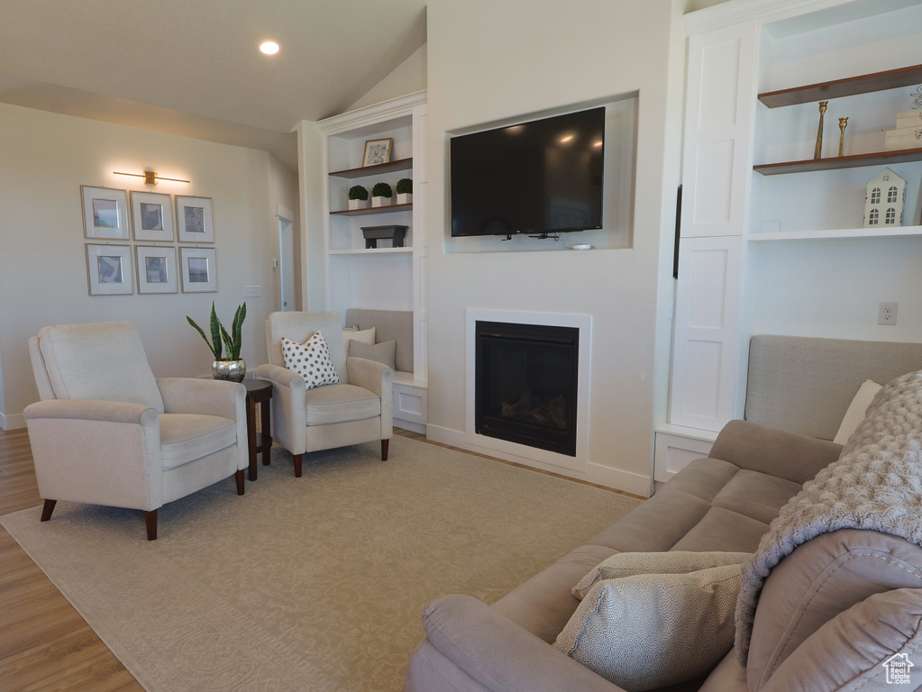 Living area featuring light wood-style flooring, a fireplace, lofted ceiling, recessed lighting, and built in features