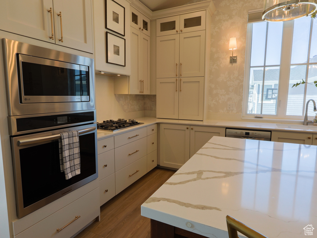Kitchen featuring appliances with stainless steel finishes, a sink, wood finished floors, white cabinetry, and wallpapered walls