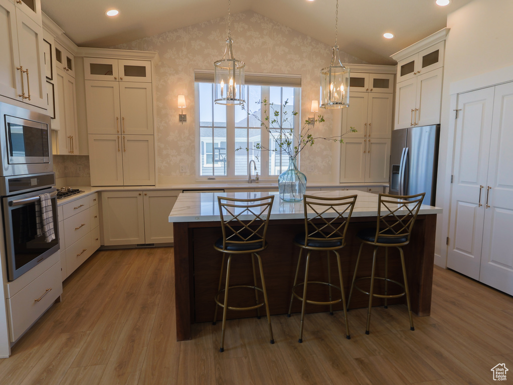 Kitchen with stainless steel appliances, vaulted ceiling, wood finished floors, light countertops, and a chandelier