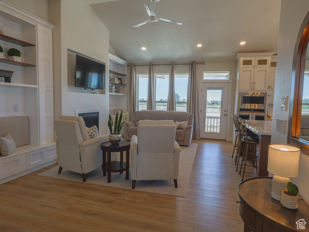 Living area featuring a fireplace, light wood-style flooring, ceiling fan, lofted ceiling, and recessed lighting
