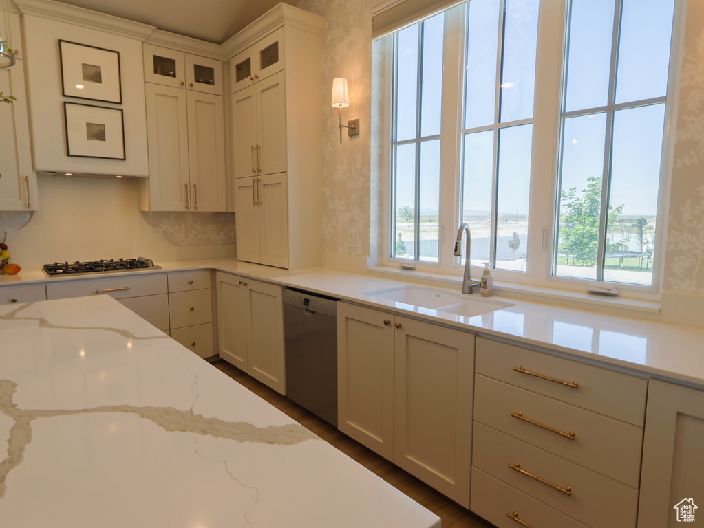 Kitchen with stainless steel dishwasher, a sink, gas stovetop, white cabinetry, and glass insert cabinets