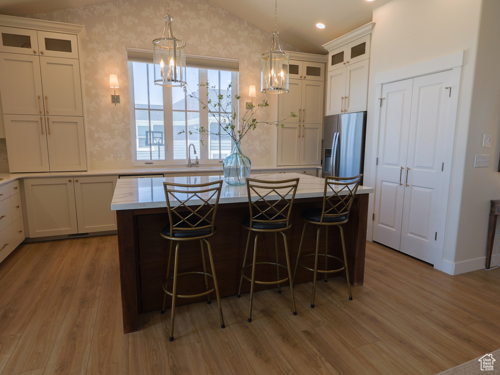 Kitchen with stainless steel fridge with ice dispenser, wood finished floors, a center island, lofted ceiling, and white cabinetry