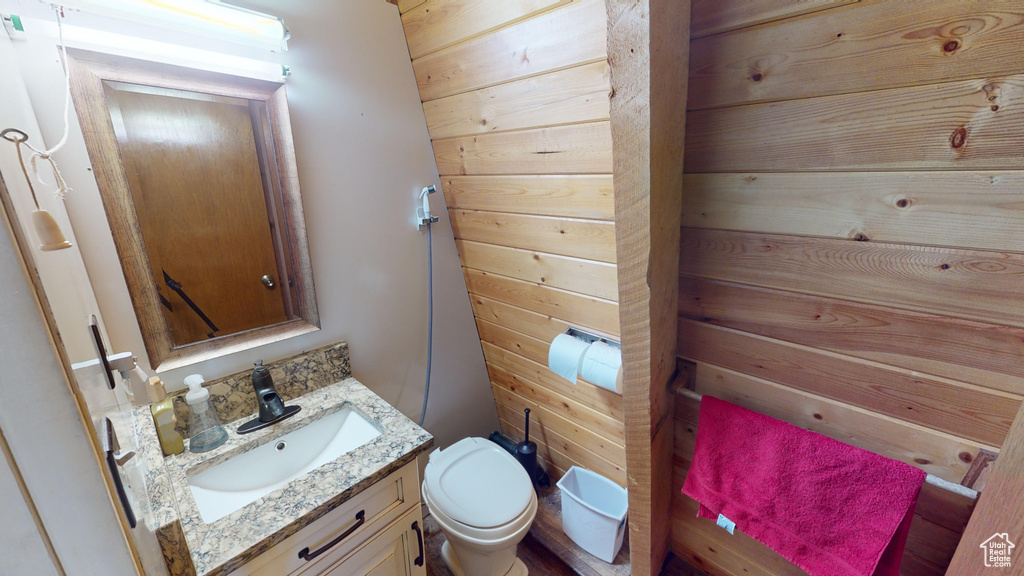Half bath with vanity, toilet, and wooden walls