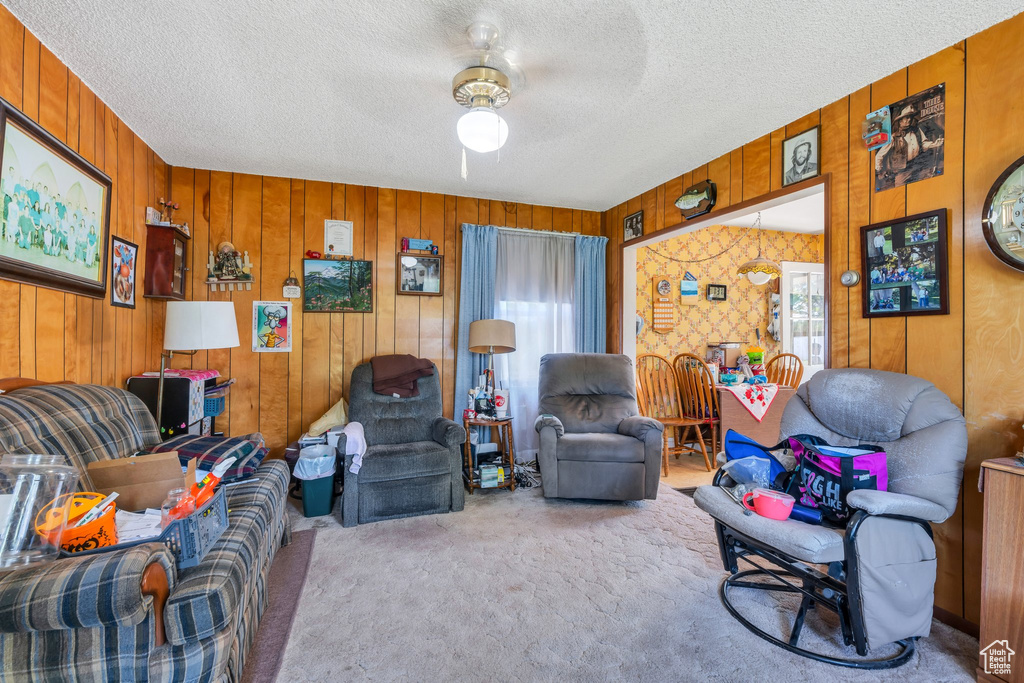 Living room with carpet floors, healthy amount of natural light, a textured ceiling, a ceiling fan, and wood walls