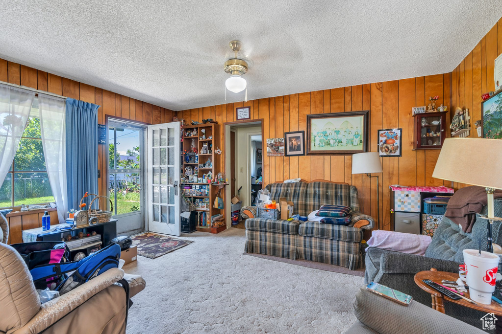 Living room featuring carpet floors, ceiling fan, wooden walls, and a textured ceiling