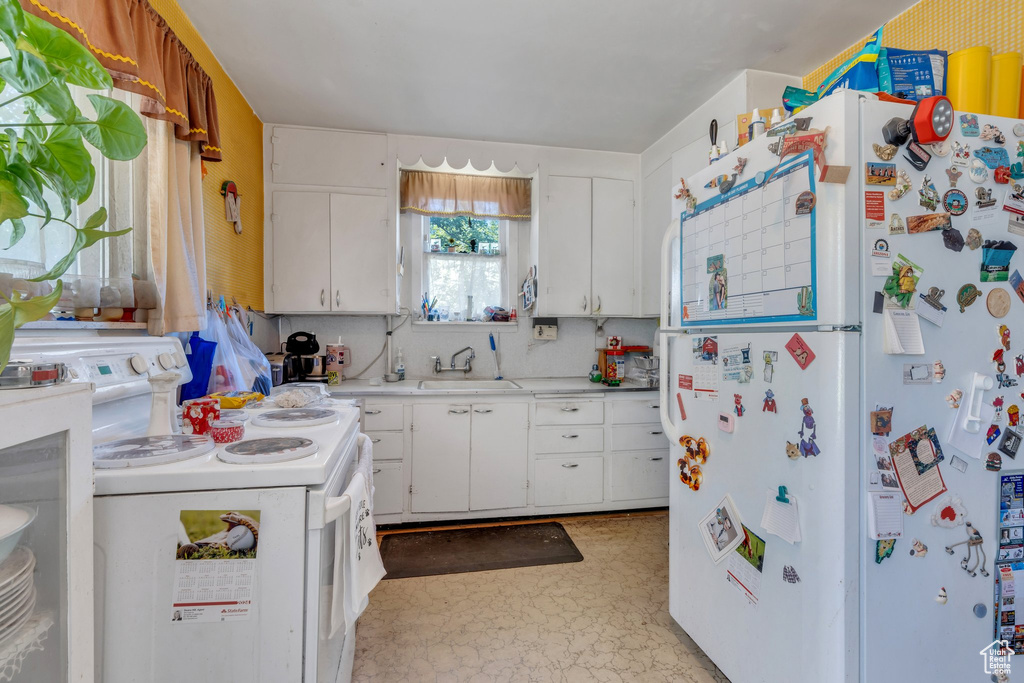 Kitchen featuring freestanding refrigerator, stove, a sink, light countertops, and white cabinetry