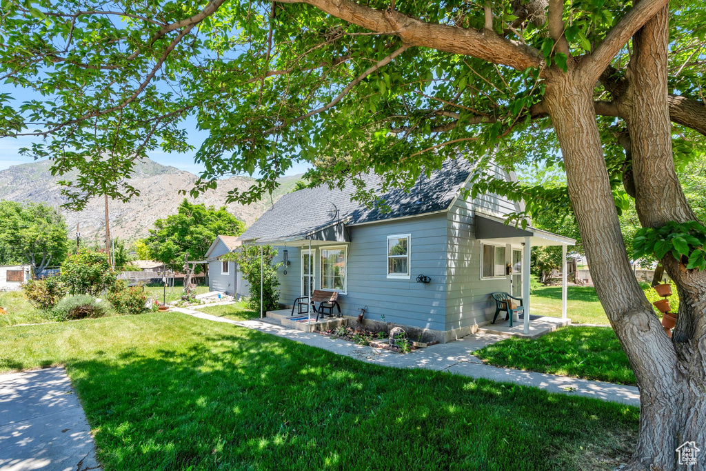 View of side of home featuring a mountain view, a yard, a patio area, and roof with shingles