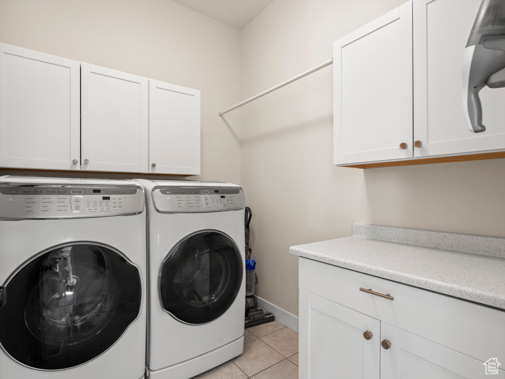 Washroom with cabinet space, separate washer and dryer, light tile patterned floors, and baseboards