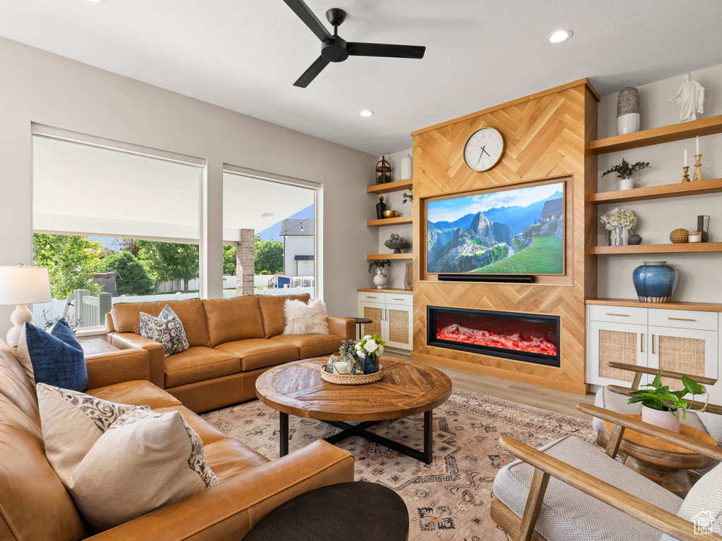 Living area featuring ceiling fan, a glass covered fireplace, wood finished floors, recessed lighting, and built in shelves