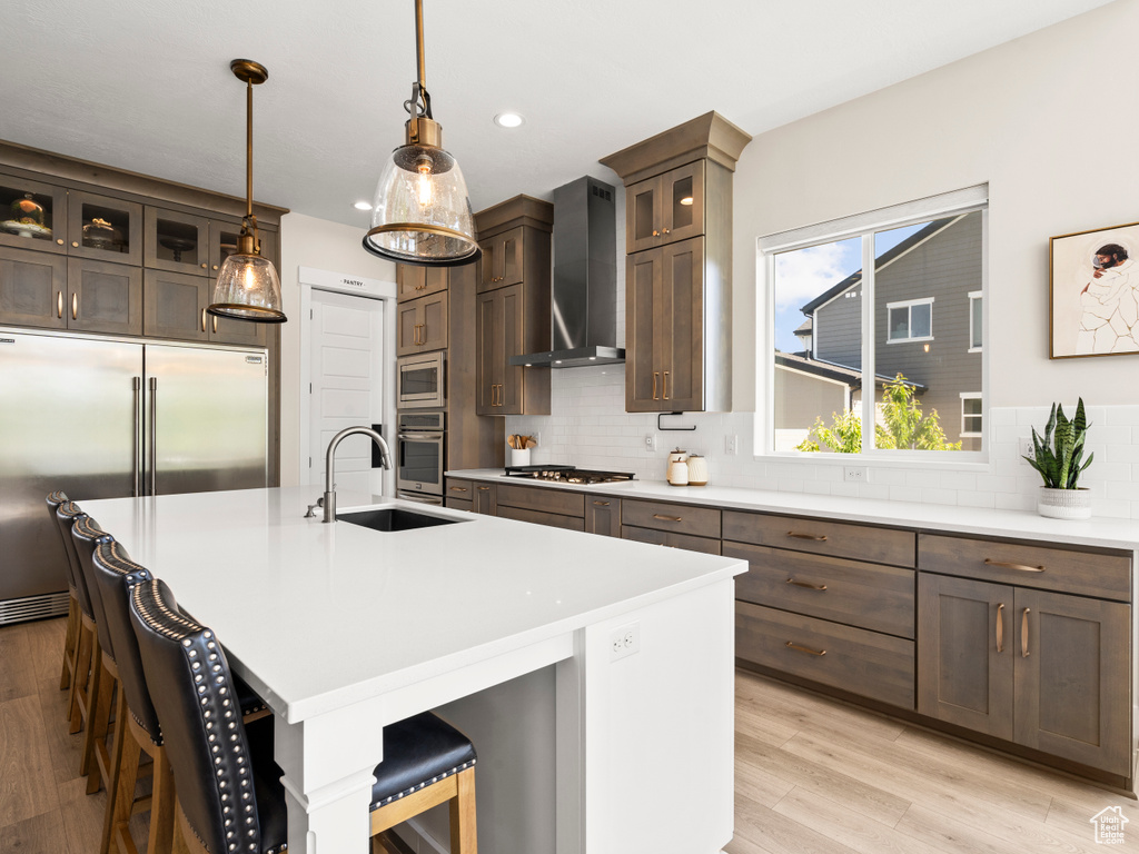 Kitchen with a sink, wall chimney exhaust hood, built in appliances, backsplash, and a kitchen breakfast bar