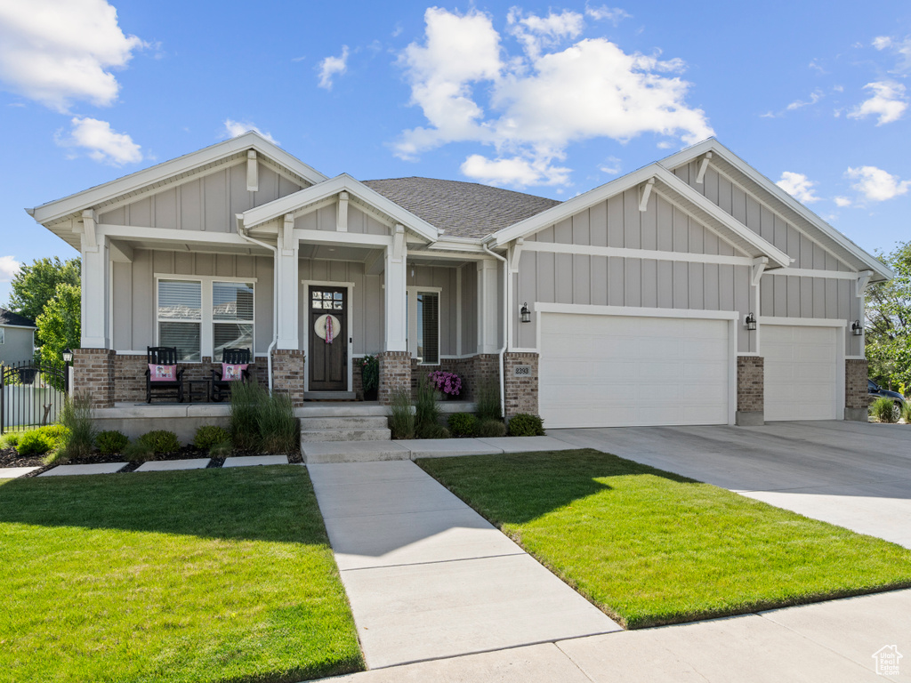 Craftsman-style home with brick siding, a garage, driveway, a front lawn, and board and batten siding