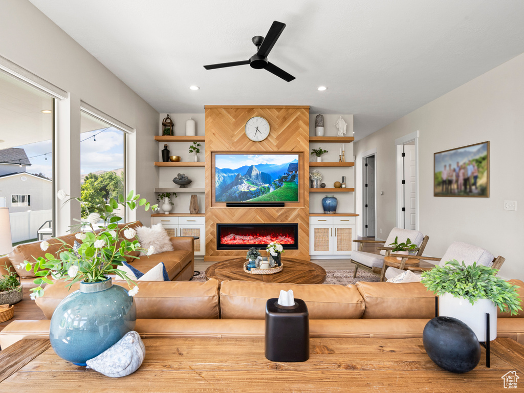 Living room featuring ceiling fan, a warm lit fireplace, and recessed lighting