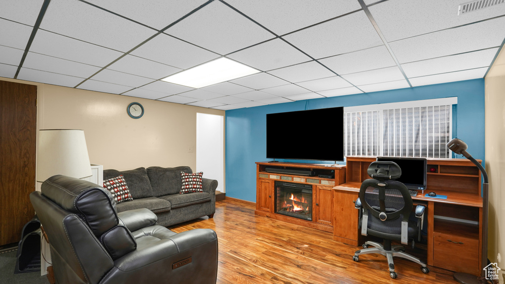 Home office with light wood-type flooring, a lit fireplace, and a paneled ceiling