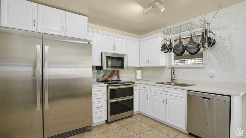 Kitchen with appliances with stainless steel finishes, a sink, light tile patterned floors, light countertops, and white cabinets