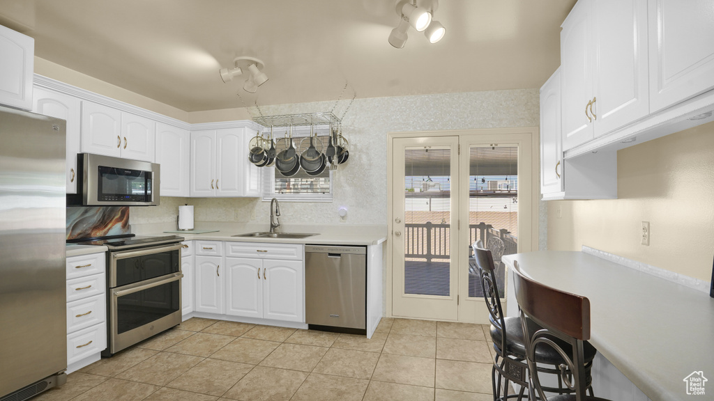 Kitchen with stainless steel appliances, a sink, light countertops, white cabinets, and light tile patterned flooring