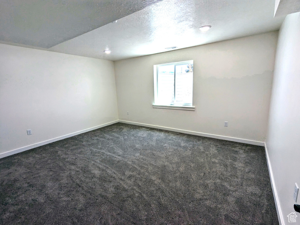 Unfurnished room featuring dark colored carpet, baseboards, and a textured ceiling