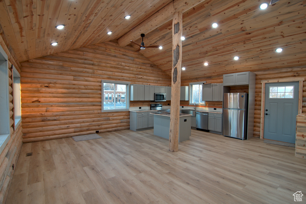 Kitchen featuring appliances with stainless steel finishes, log walls, gray cabinetry, a ceiling fan, and light wood-style floors