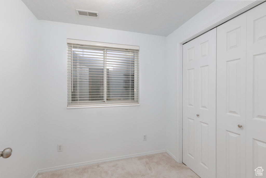Unfurnished bedroom with a closet, light carpet, and baseboards