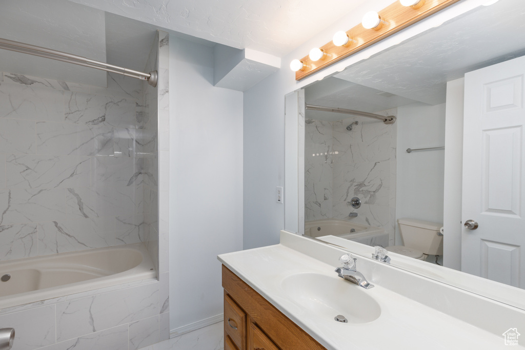 Bathroom with a combined bath / shower with marble appearance, vanity, toilet, marble finish flooring, and baseboards