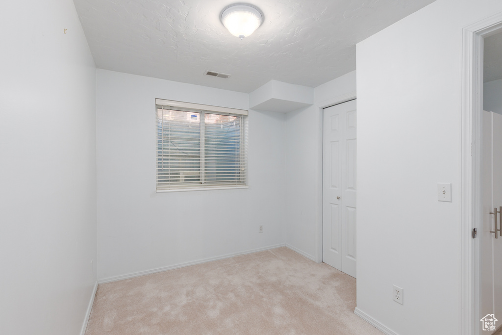 Unfurnished bedroom featuring light carpet, a textured ceiling, baseboards, and a closet