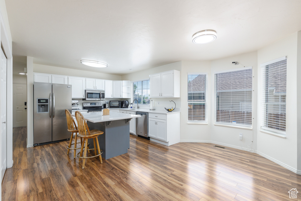 Kitchen featuring appliances with stainless steel finishes, white cabinetry, light countertops, a kitchen island, and a kitchen bar