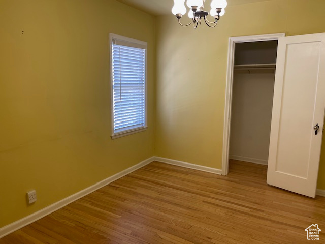 Unfurnished bedroom featuring a chandelier, baseboards, wood finished floors, and a closet
