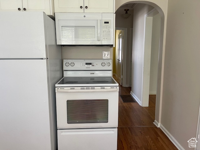 Kitchen with white appliances, arched walkways, dark wood-type flooring, baseboards, and white cabinetry