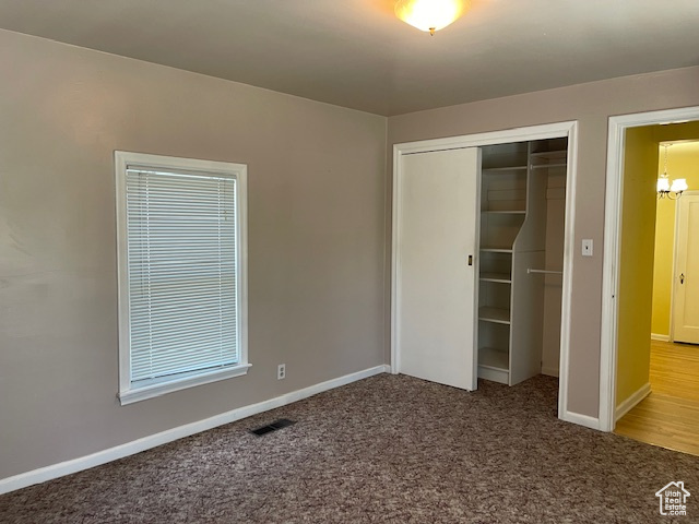 Unfurnished bedroom featuring carpet floors, a closet, a chandelier, and baseboards