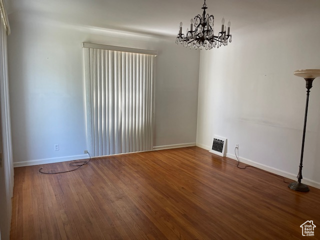 Unfurnished room featuring a chandelier, baseboards, and wood finished floors