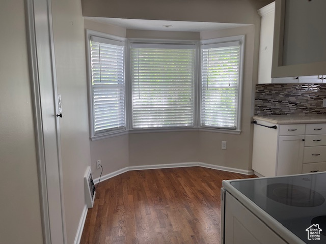Kitchen featuring electric range oven, white cabinets, wood finished floors, decorative backsplash, and healthy amount of natural light