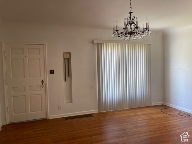 Spare room with wood finished floors, baseboards, and a chandelier
