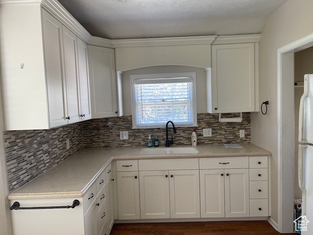 Kitchen with a sink, freestanding refrigerator, white cabinets, and decorative backsplash