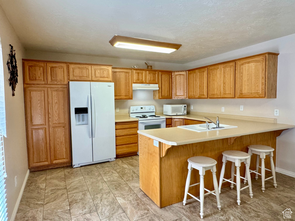 Kitchen featuring white appliances, a sink, under cabinet range hood, and baseboards