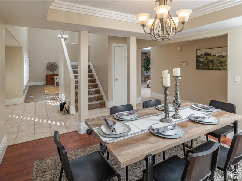 Dining room with a chandelier, light wood-style flooring, stairs, a raised ceiling, and baseboards
