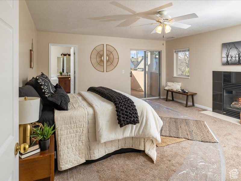 Carpeted bedroom featuring access to outside, a tiled fireplace, a ceiling fan, ensuite bath, and baseboards
