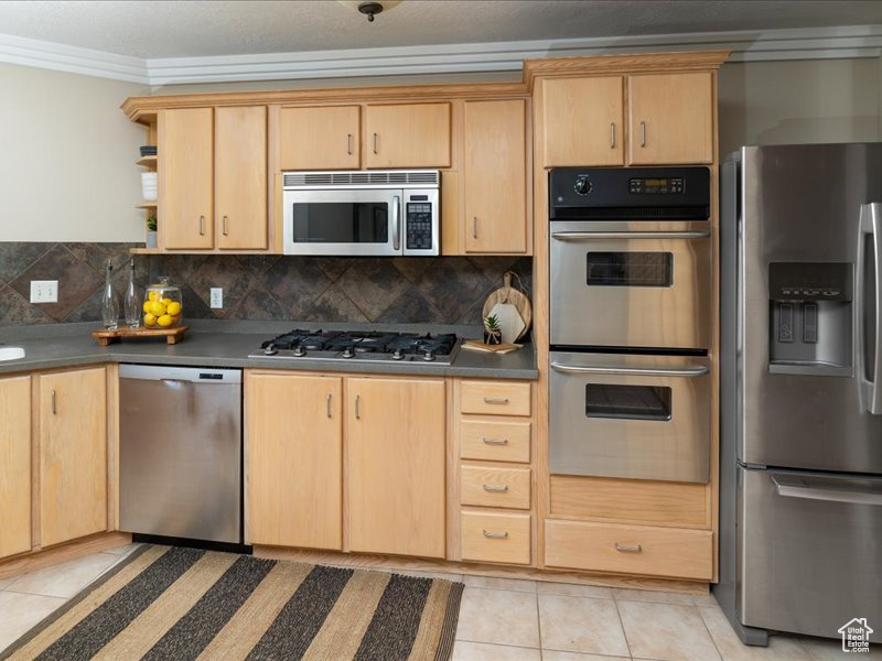 Kitchen featuring appliances with stainless steel finishes, ornamental molding, open shelves, light brown cabinetry, and light tile patterned flooring