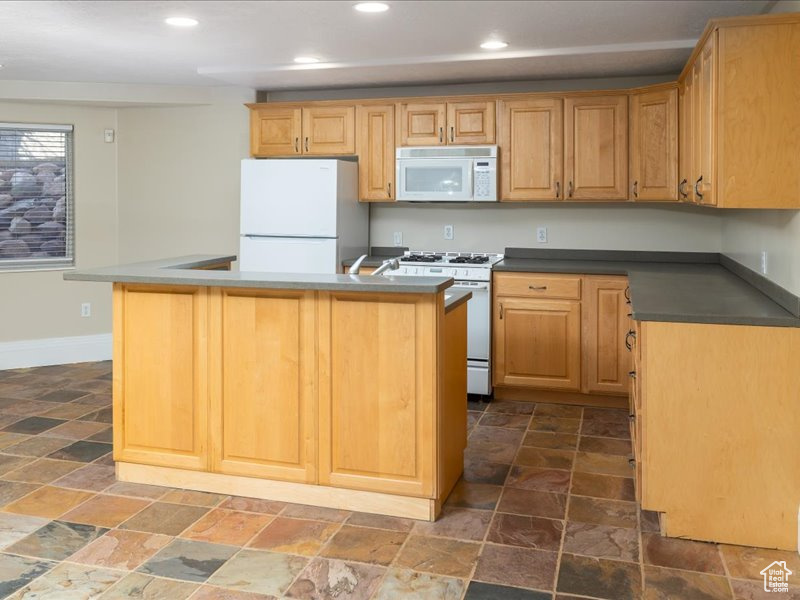 Kitchen with white appliances, stone tile flooring, recessed lighting, baseboards, and dark countertops