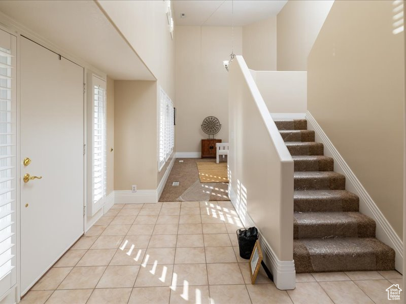 Foyer featuring a towering ceiling, light tile patterned flooring, stairway, and baseboards
