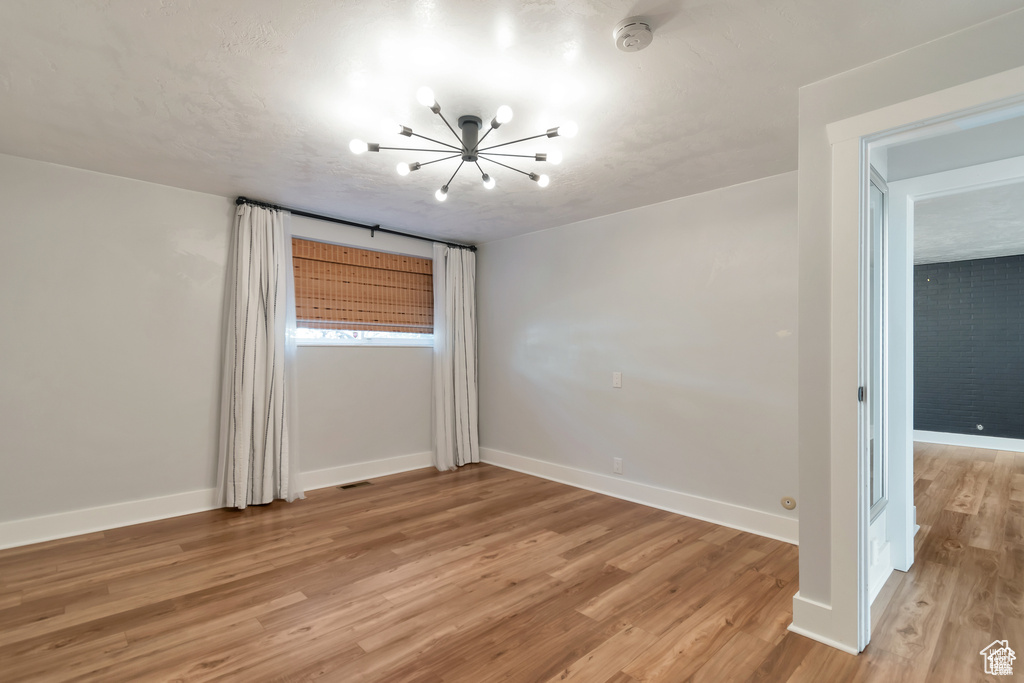 Empty room with a chandelier, light wood-style flooring, baseboards, and a smoke detector