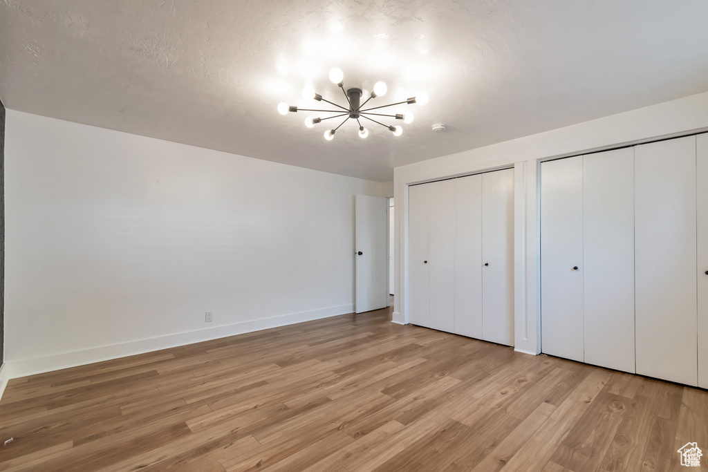 Unfurnished bedroom featuring two closets, light wood-style floors, a chandelier, and baseboards