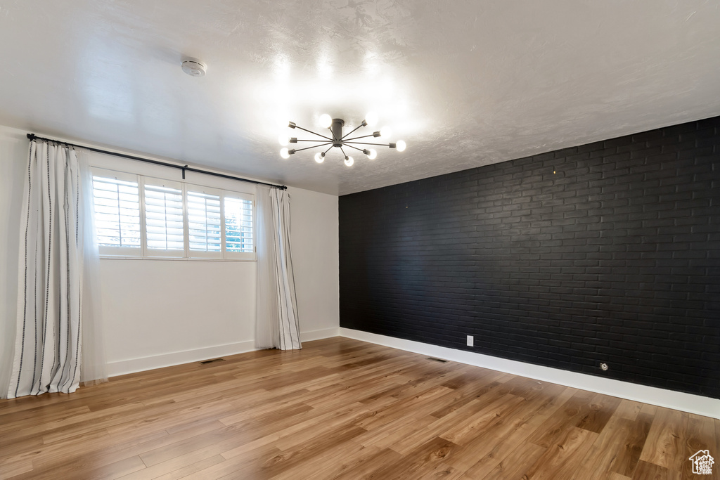 Unfurnished room featuring a chandelier, brick wall, baseboards, a smoke detector, and light wood-style flooring