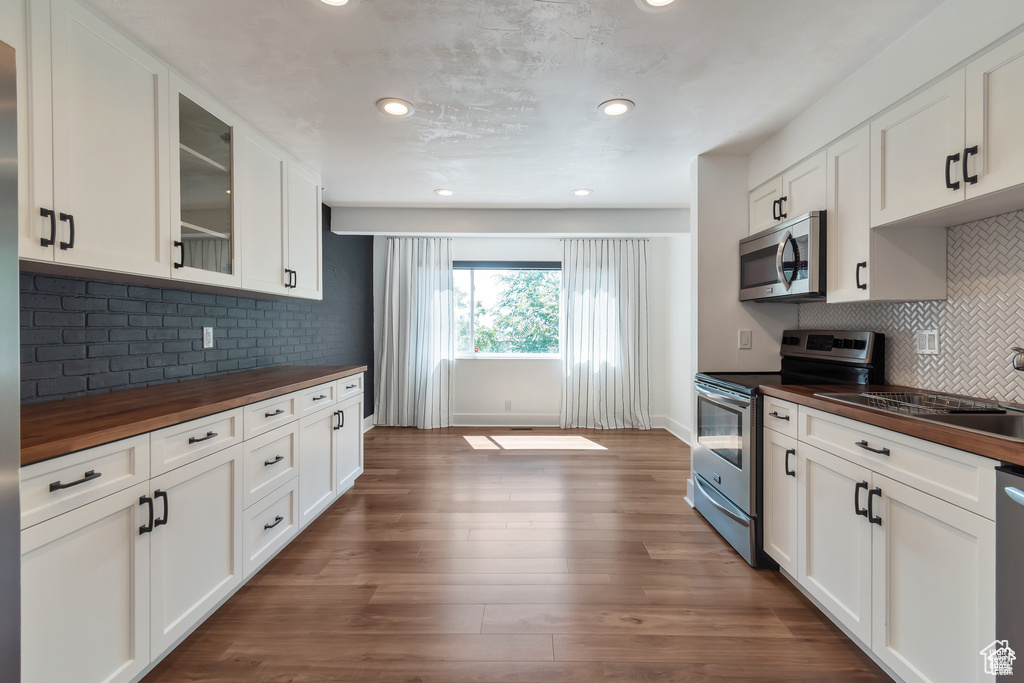 Kitchen with wooden counters, appliances with stainless steel finishes, glass insert cabinets, backsplash, and dark wood finished floors
