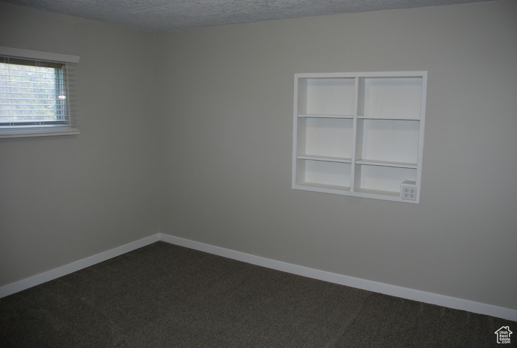 Spare room with dark carpet, a textured ceiling, and baseboards