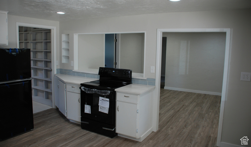 Kitchen with black appliances, wood finished floors, light countertops, white cabinets, and a textured ceiling