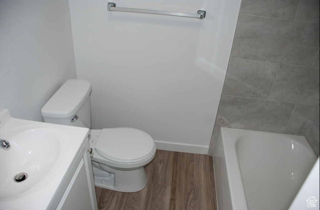 Full bath with wood finished floors, a tub, toilet, vanity, and baseboards