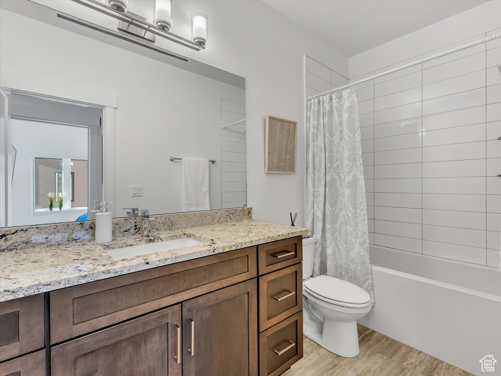 Bathroom featuring wood finished floors, vanity, toilet, and shower / bathtub combination with curtain