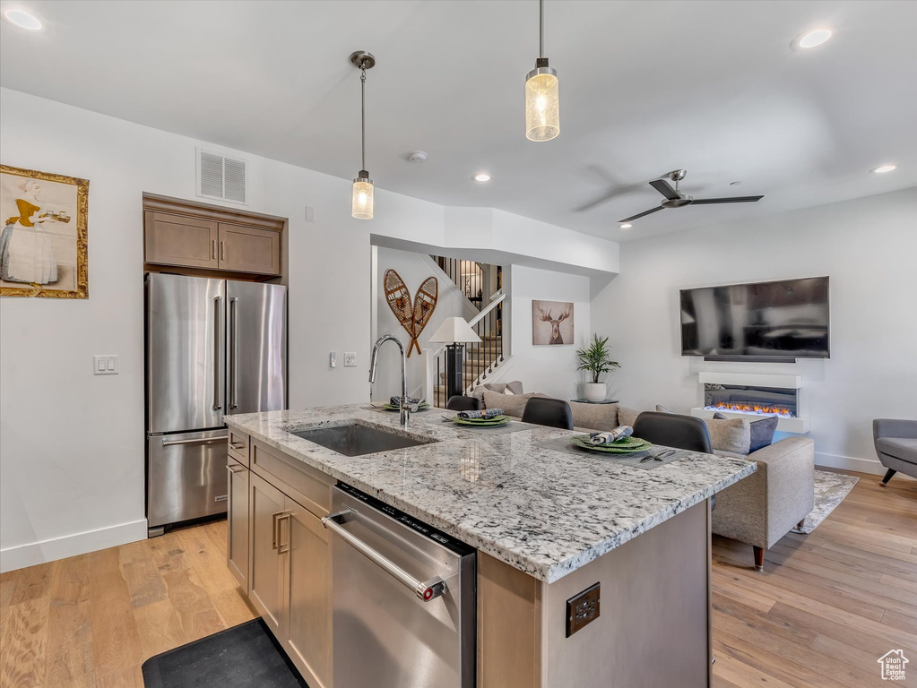 Kitchen featuring appliances with stainless steel finishes, a sink, open floor plan, light stone counters, and an island with sink