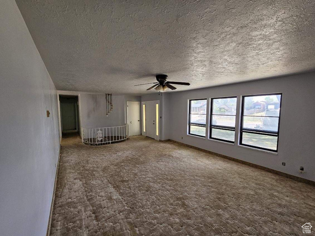 Carpeted spare room featuring ceiling fan, a textured ceiling, and baseboards
