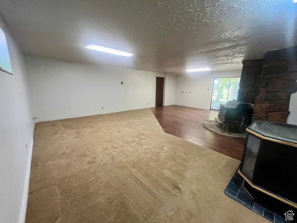 Carpeted living room featuring a wood stove, a textured ceiling, and wood finished floors