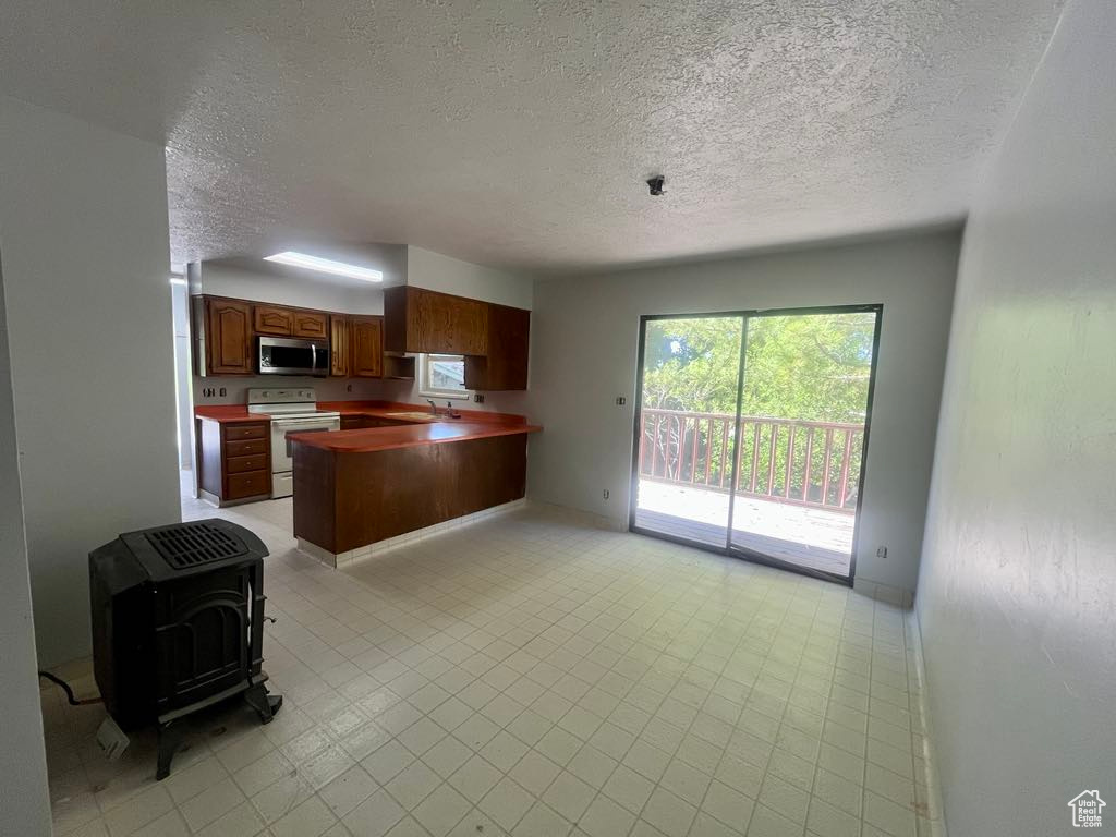Kitchen with stainless steel microwave, a textured ceiling, white range with electric cooktop, a peninsula, and open floor plan